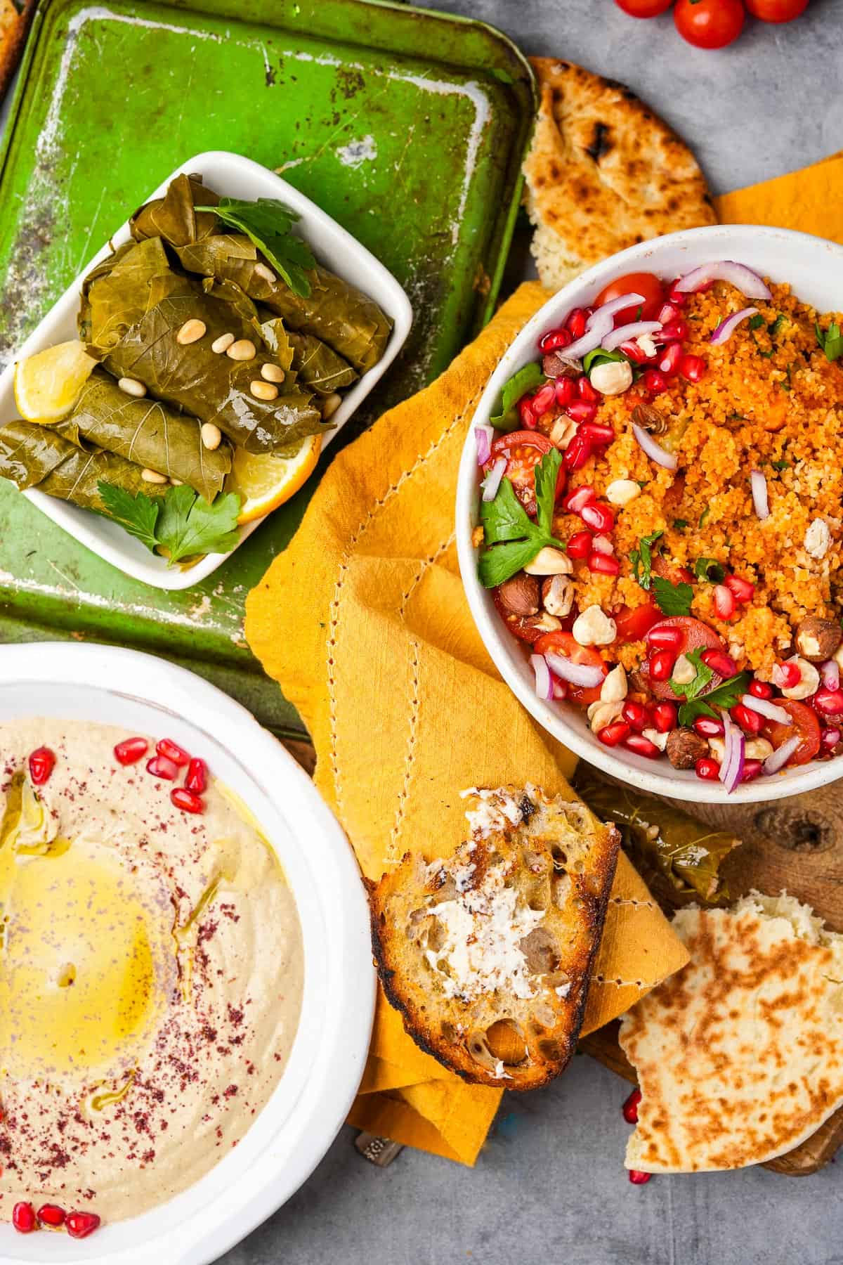 Mutabal, pita bread, stuffed grape leaves, and kisir salad on a table.