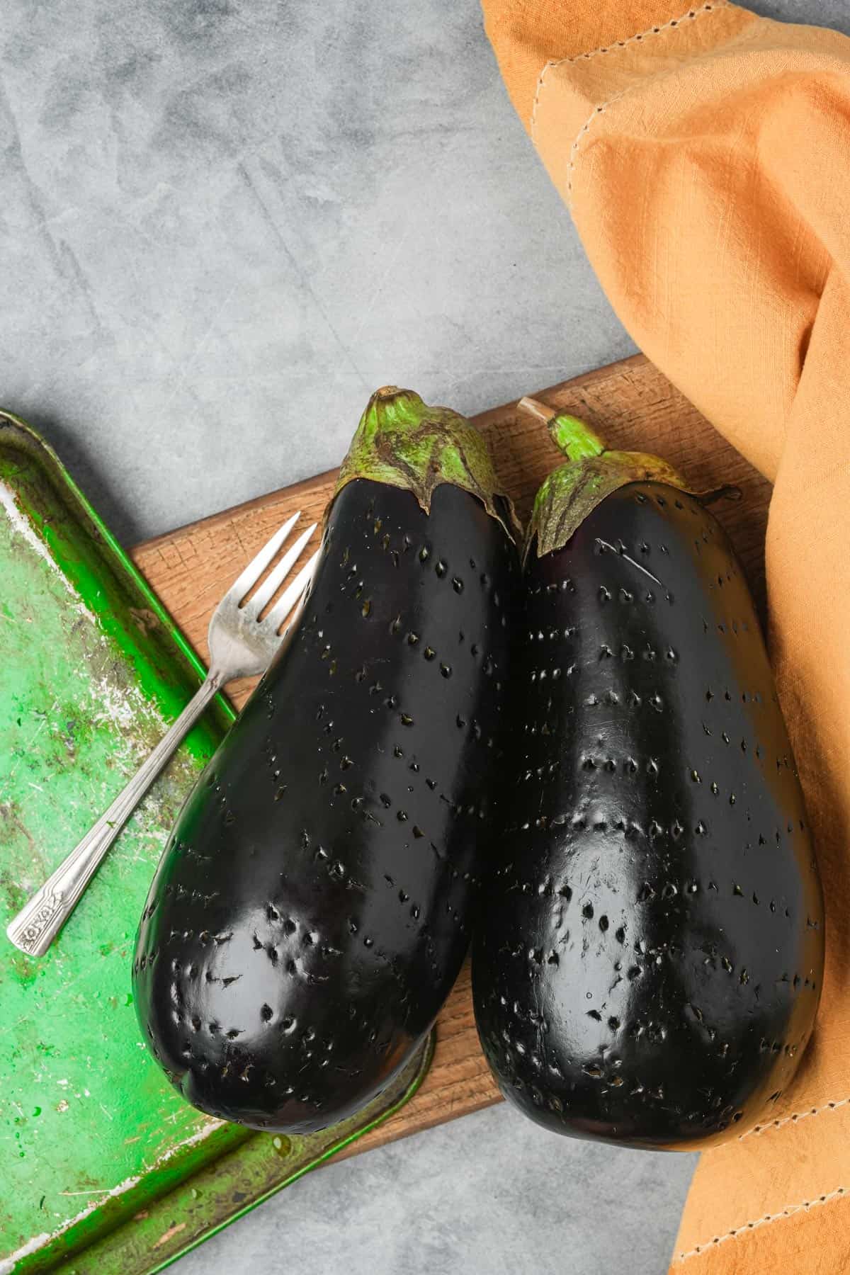 Two black eggplants pierced all over with fork pricks on a tray.