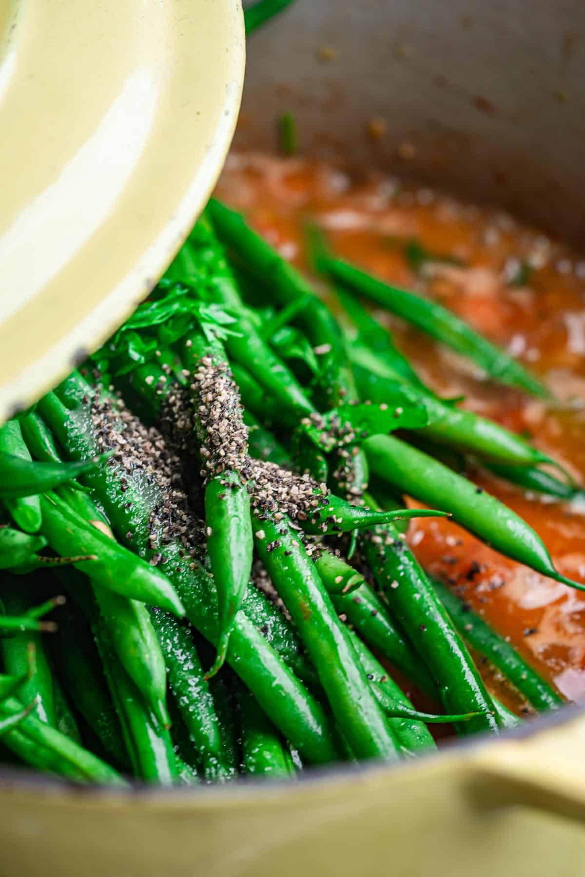 A cover being placed over green beans in a pot with spices.