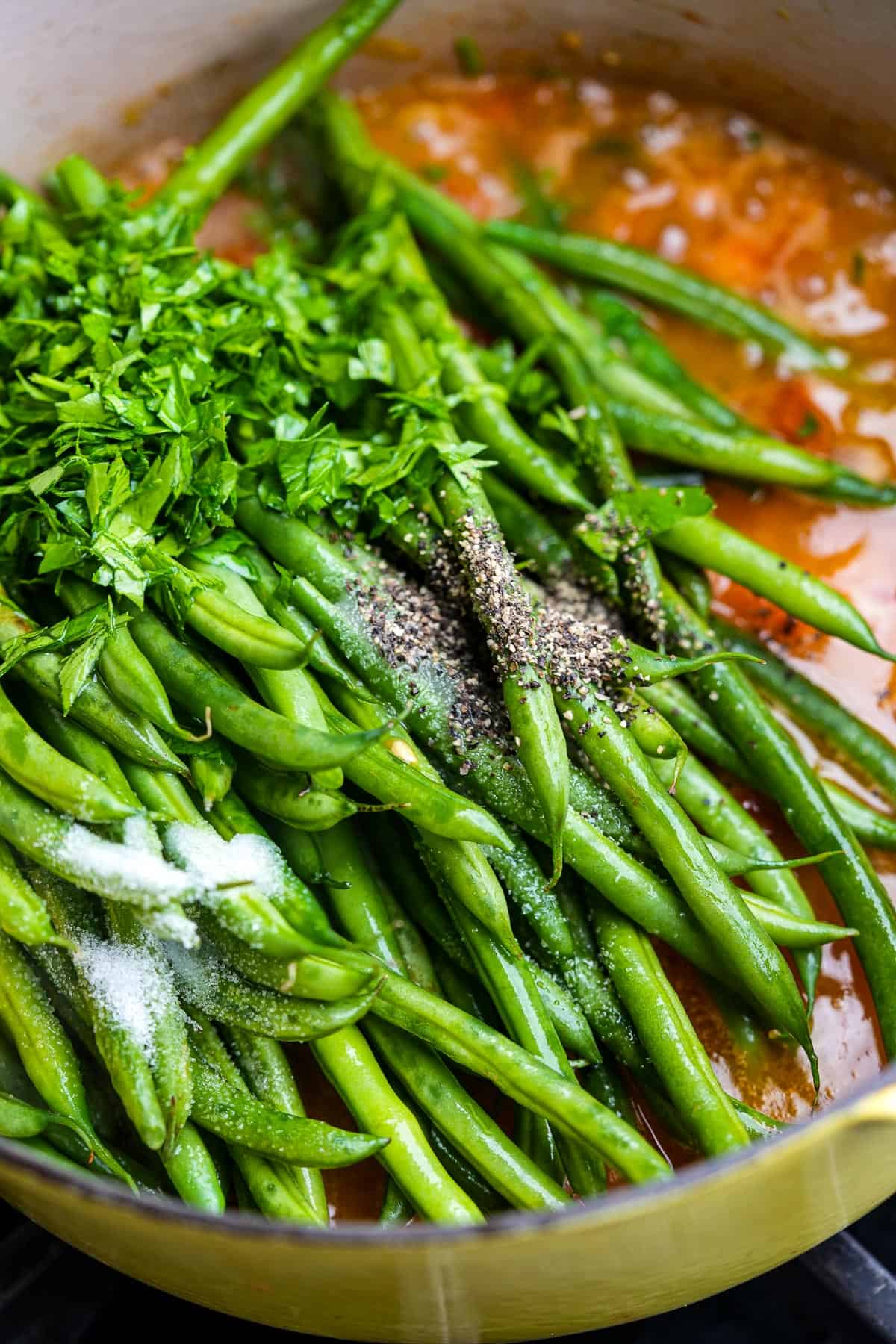Green beans steaming in a sauce with parsley on a stove.