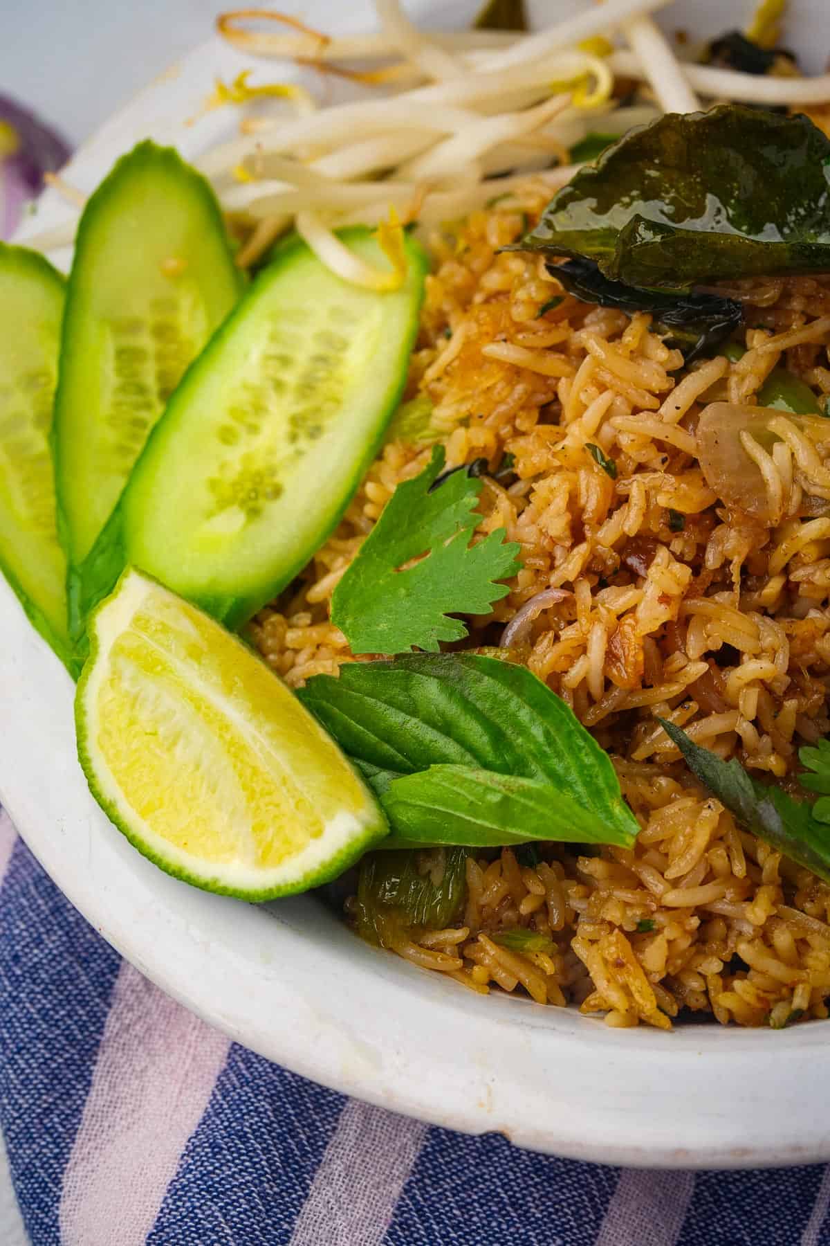 Khao pad fried rice on a plate with cucumbers and limes.