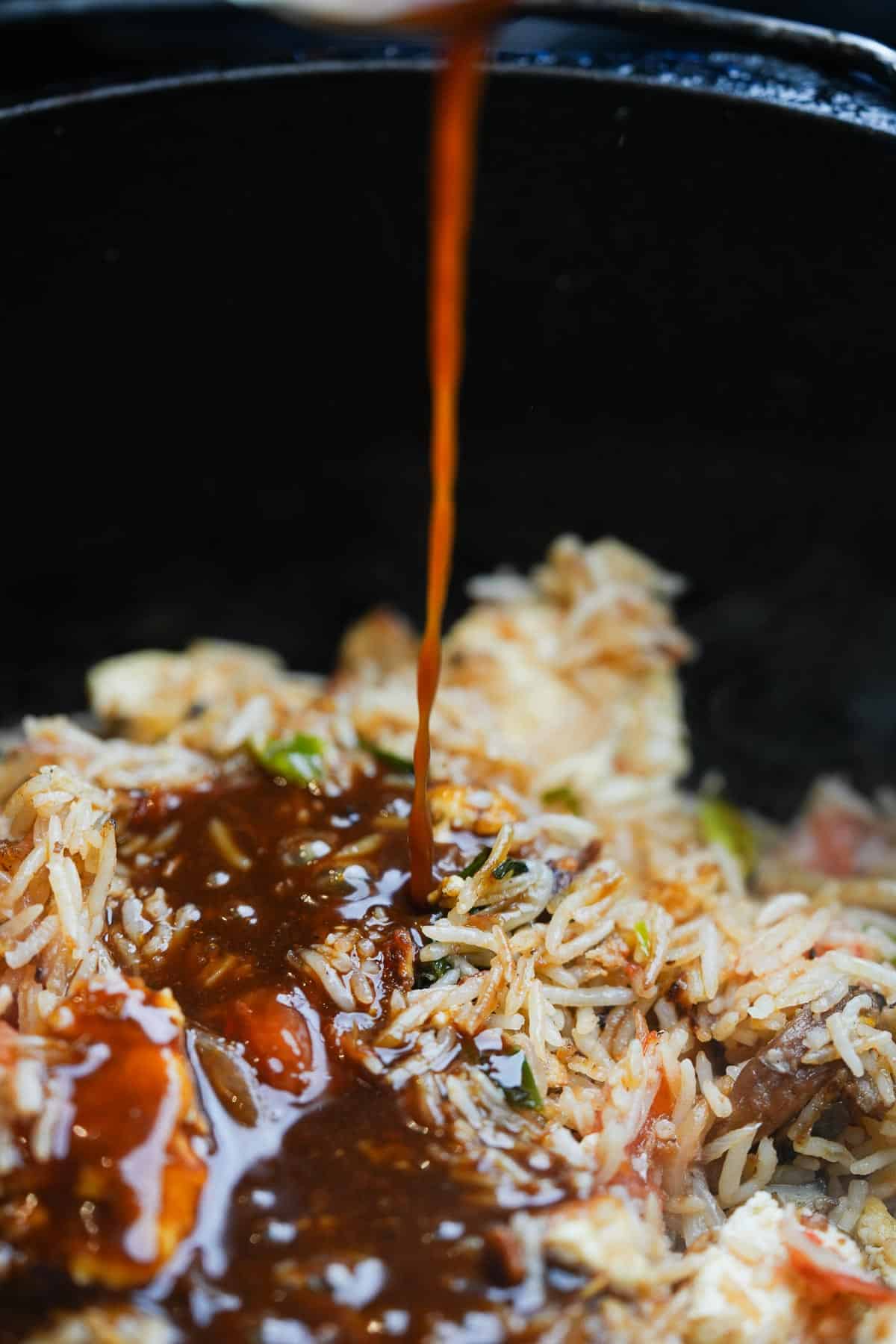 Fried rice being drizzled with stir-fry sauce.