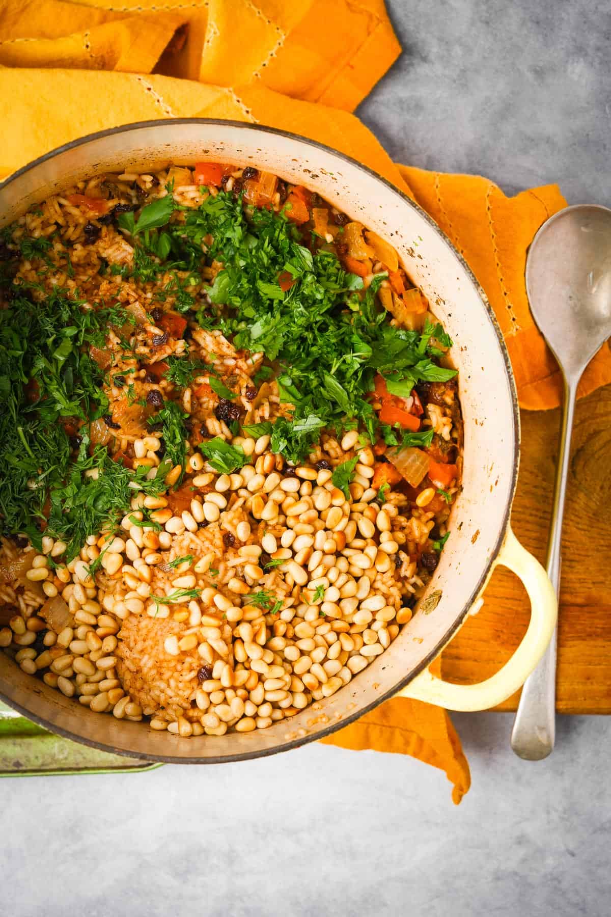 Herbs and toasted pine nuts are mixed into the cooked rice filling in a pot.