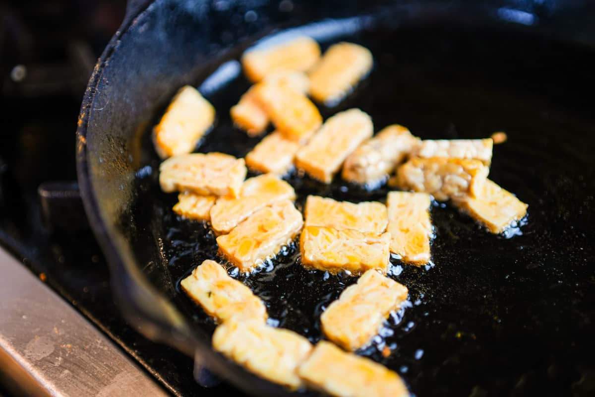 tempeh being cooked in a frying pan on the stove top.