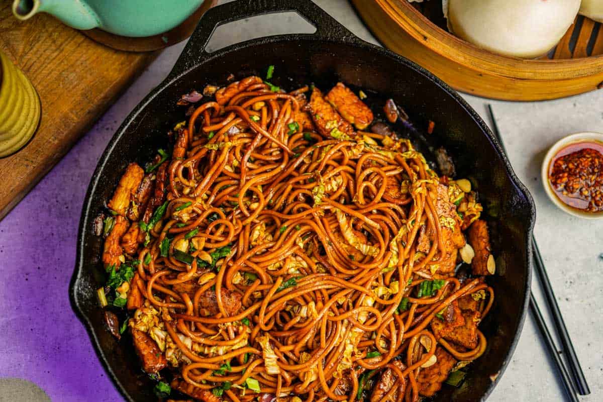 Mie goreng in a cast iron skillet on a table. tea an tea cup in the background.