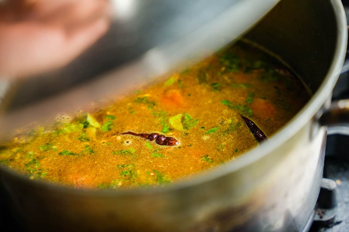 A pot of dahl is cooking on the stove. A lid is being placed on top