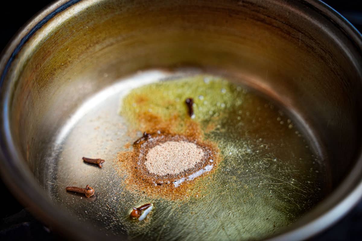 Cloves and cardamom frying in oil in a stainless steel saucepan.