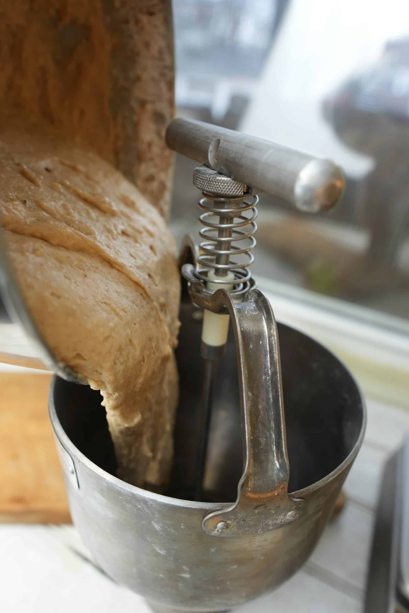 a metal mixing bowl pouring apple cider donut battering into a donut dropper.