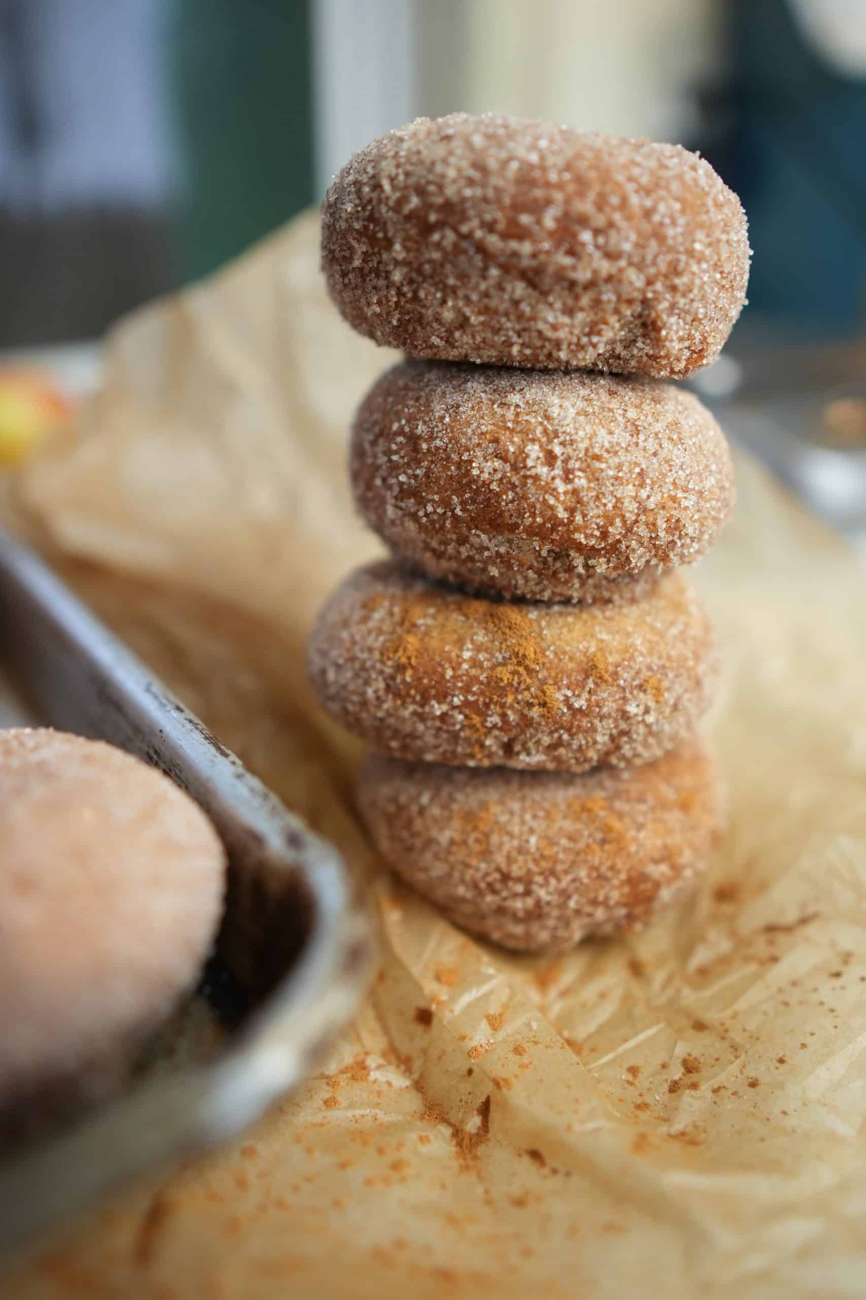 Apple cider donuts stacked up on top of each other on wax paper.