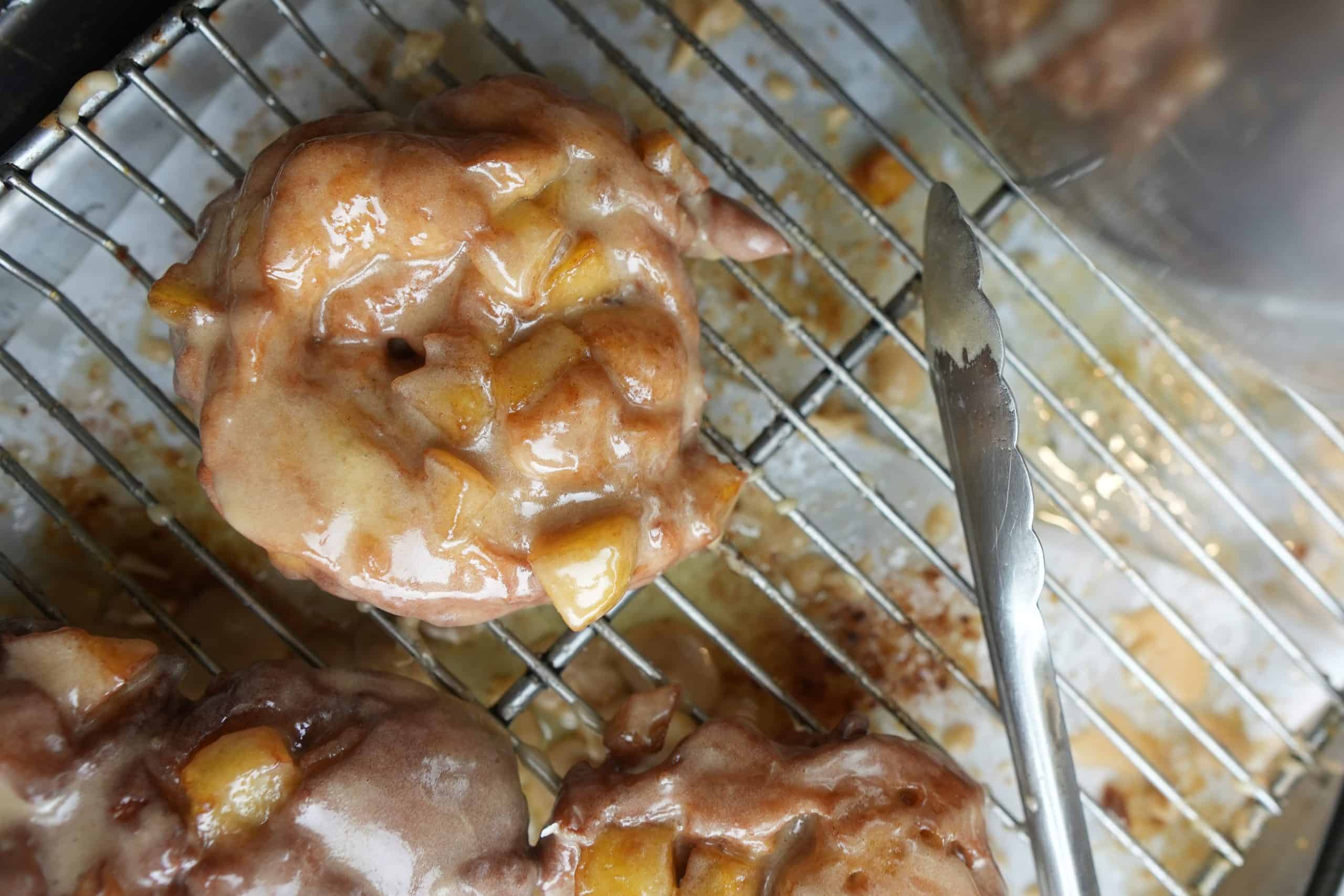 apple fritters cooling on a wire rack with a glaze covered set of tongs to the side