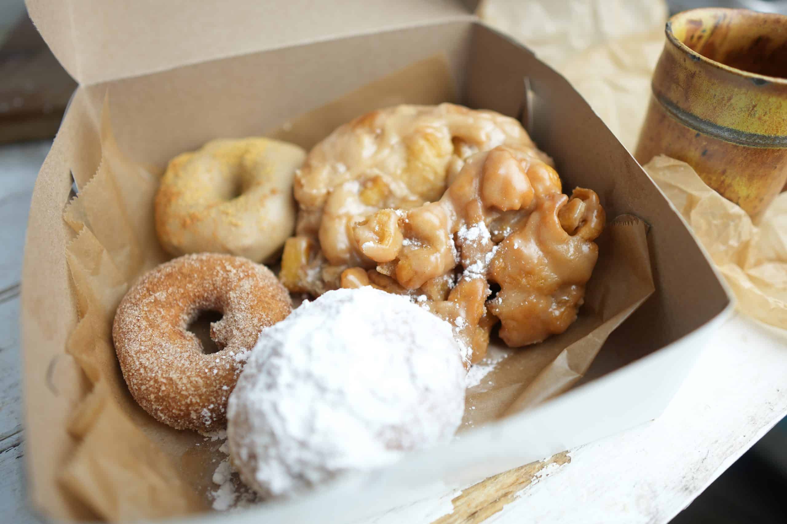 Apple cider glazed apple fritter in a pastry box along with other fresh vegan donuts
