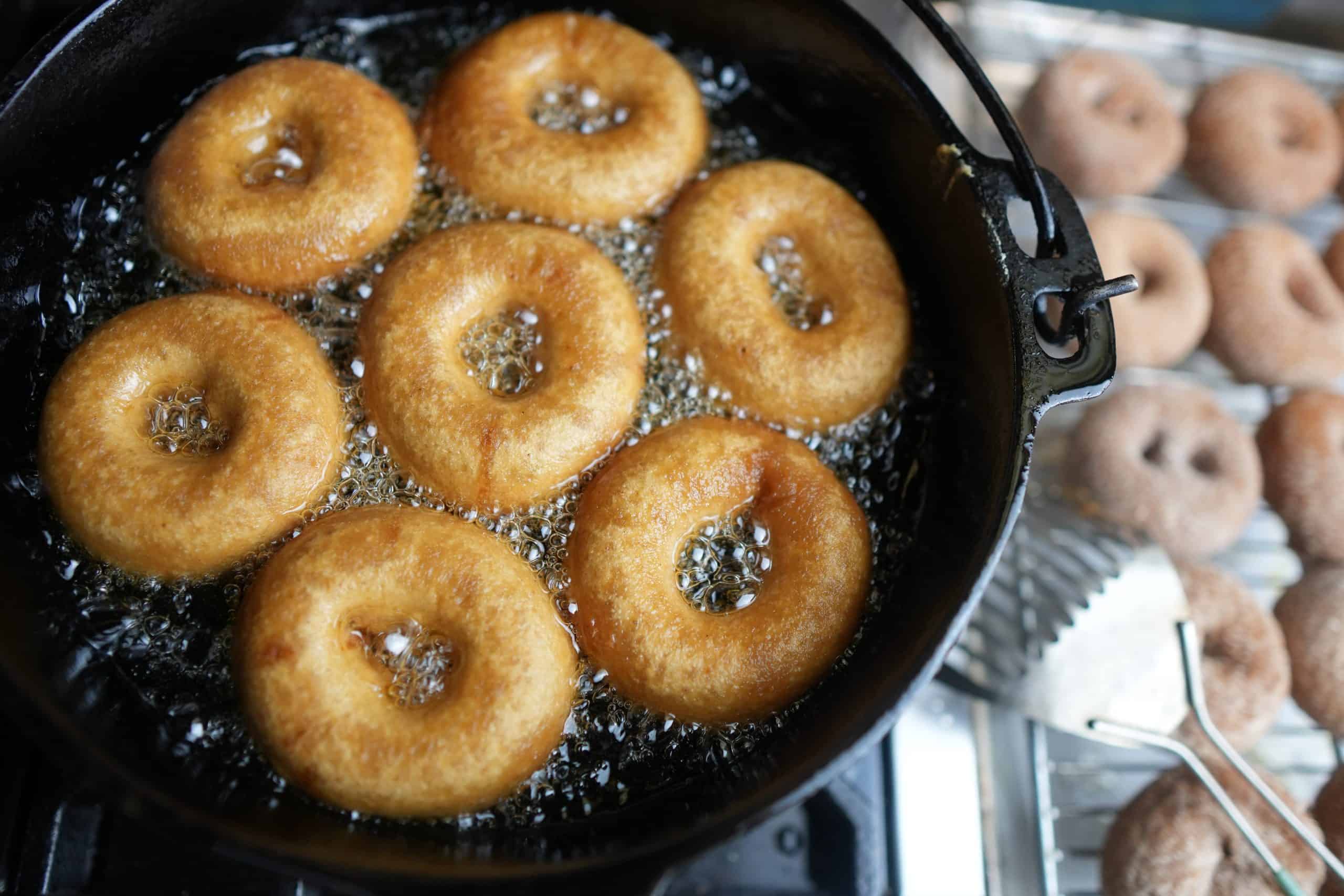Vegan apple cider donuts are being cooked in a cast iron skillet.