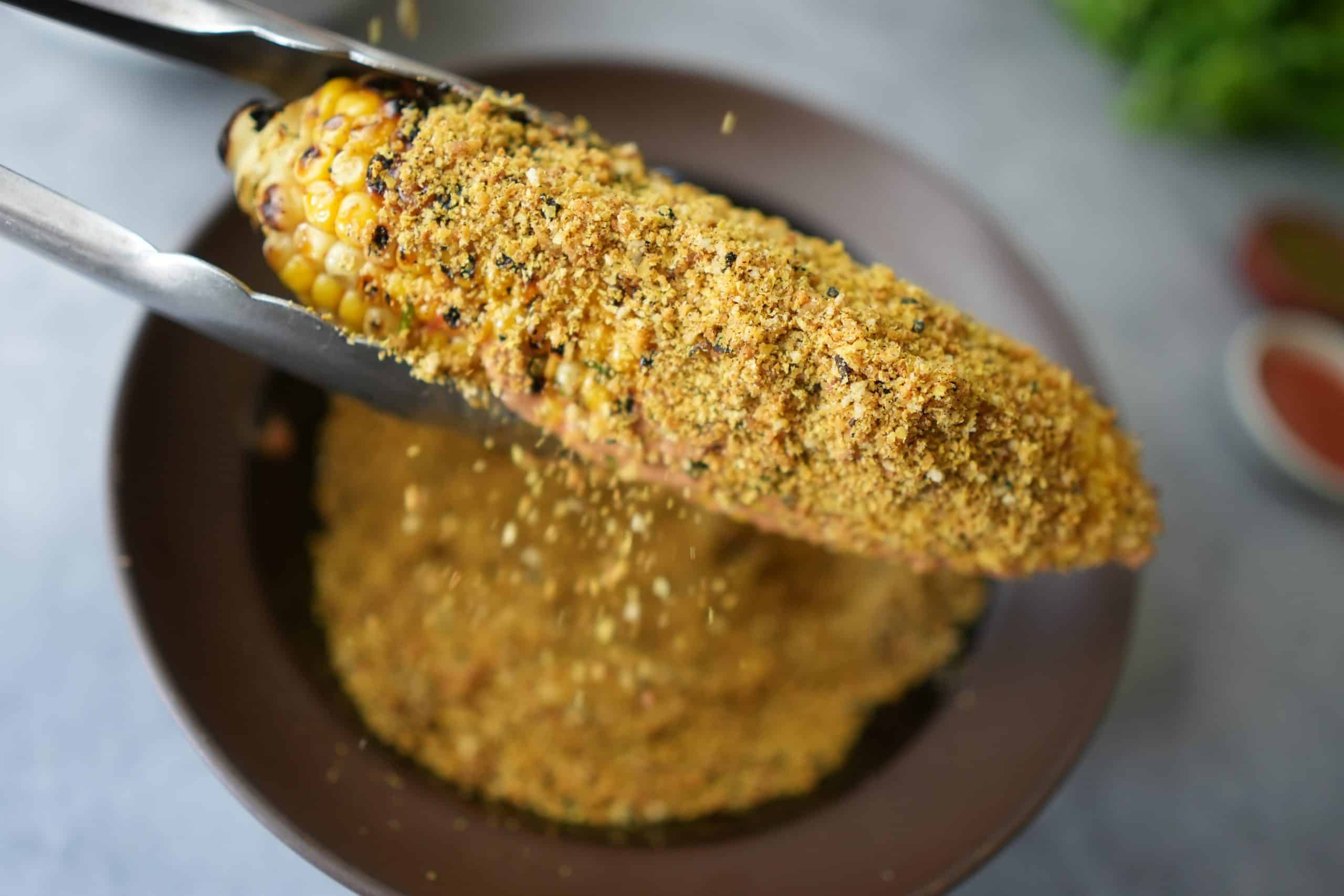 vegan elote getting coated with brazil nut cheese coating over a bowl