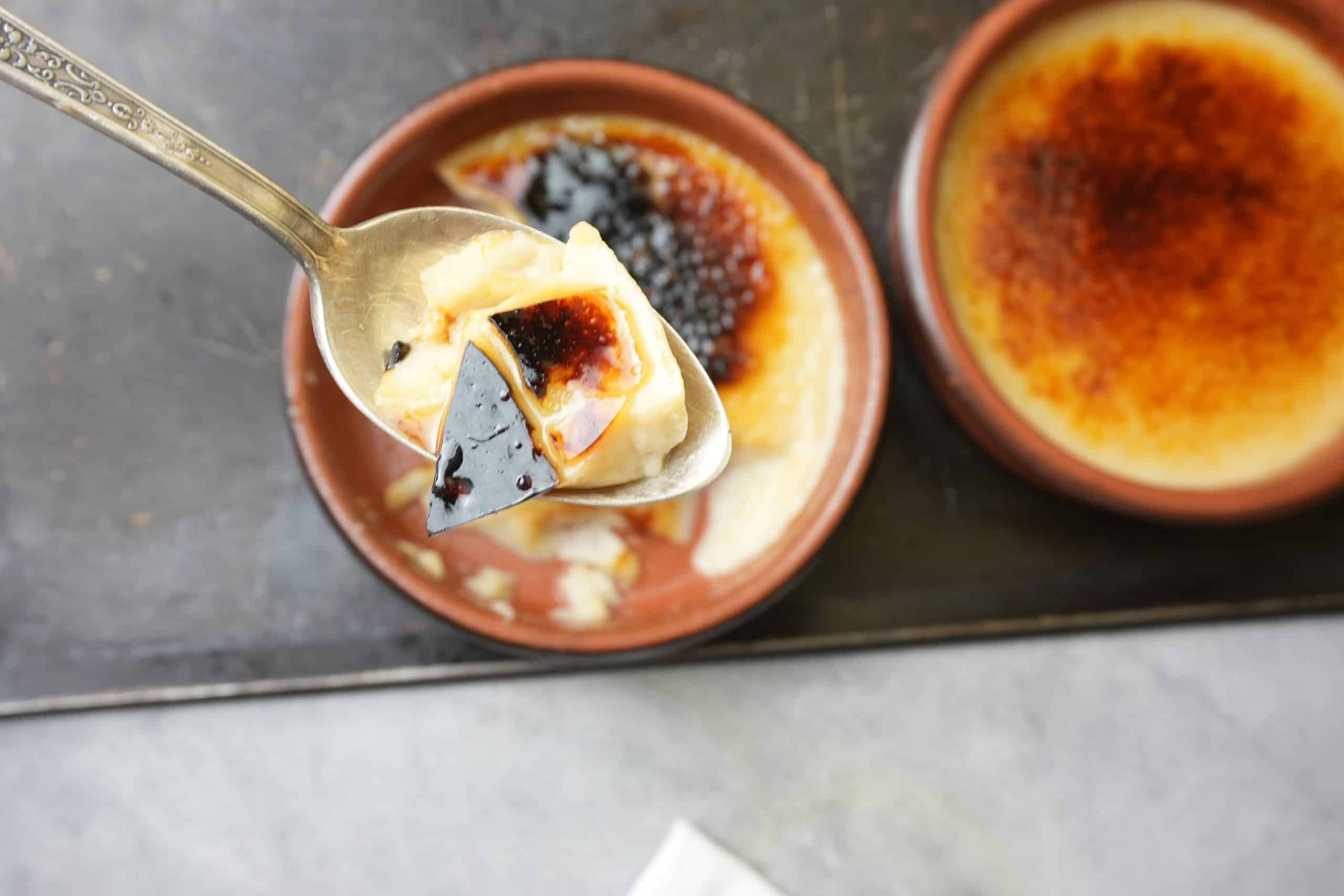 a spoonful of creme brulee up close with two torched custards in the background