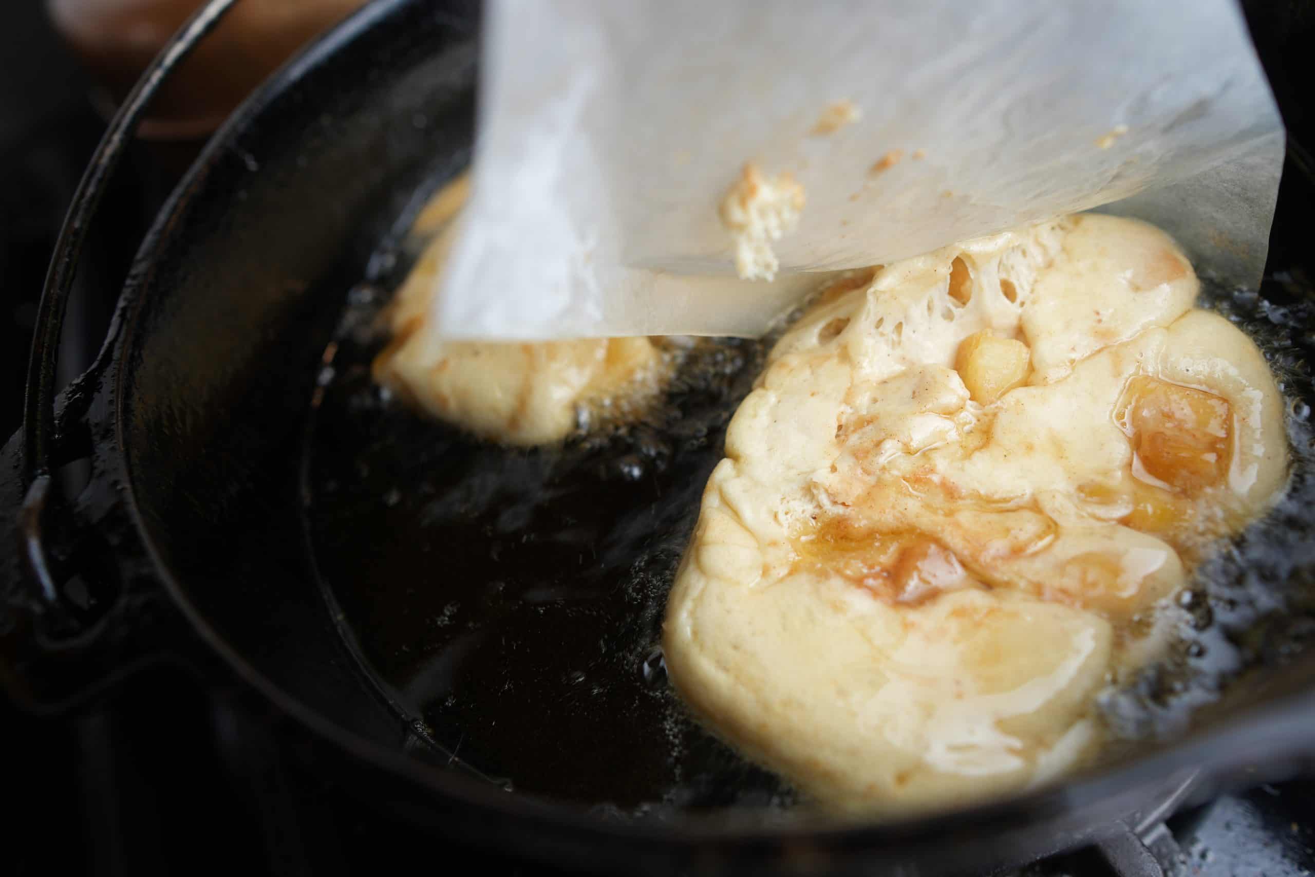 Peeling parchment off of an apple fritter as it enters the hot oil in a dutch oven.