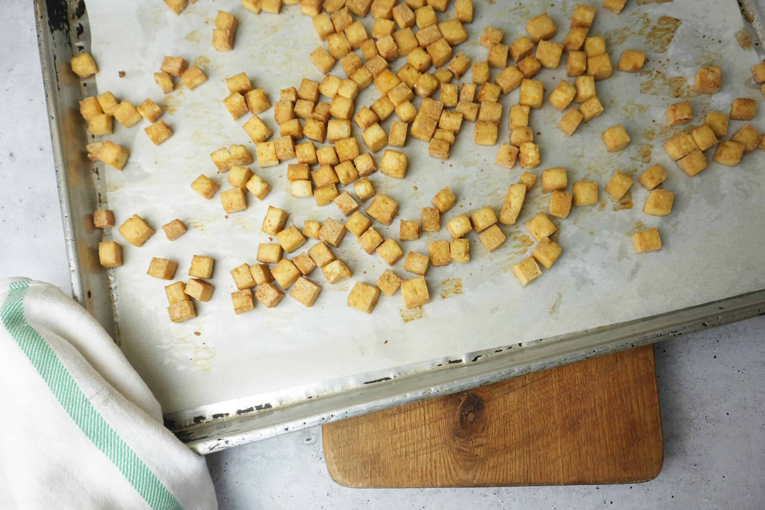 Golden brown, crispy roasted tofu cubes on a parchment paper lined baking pan.