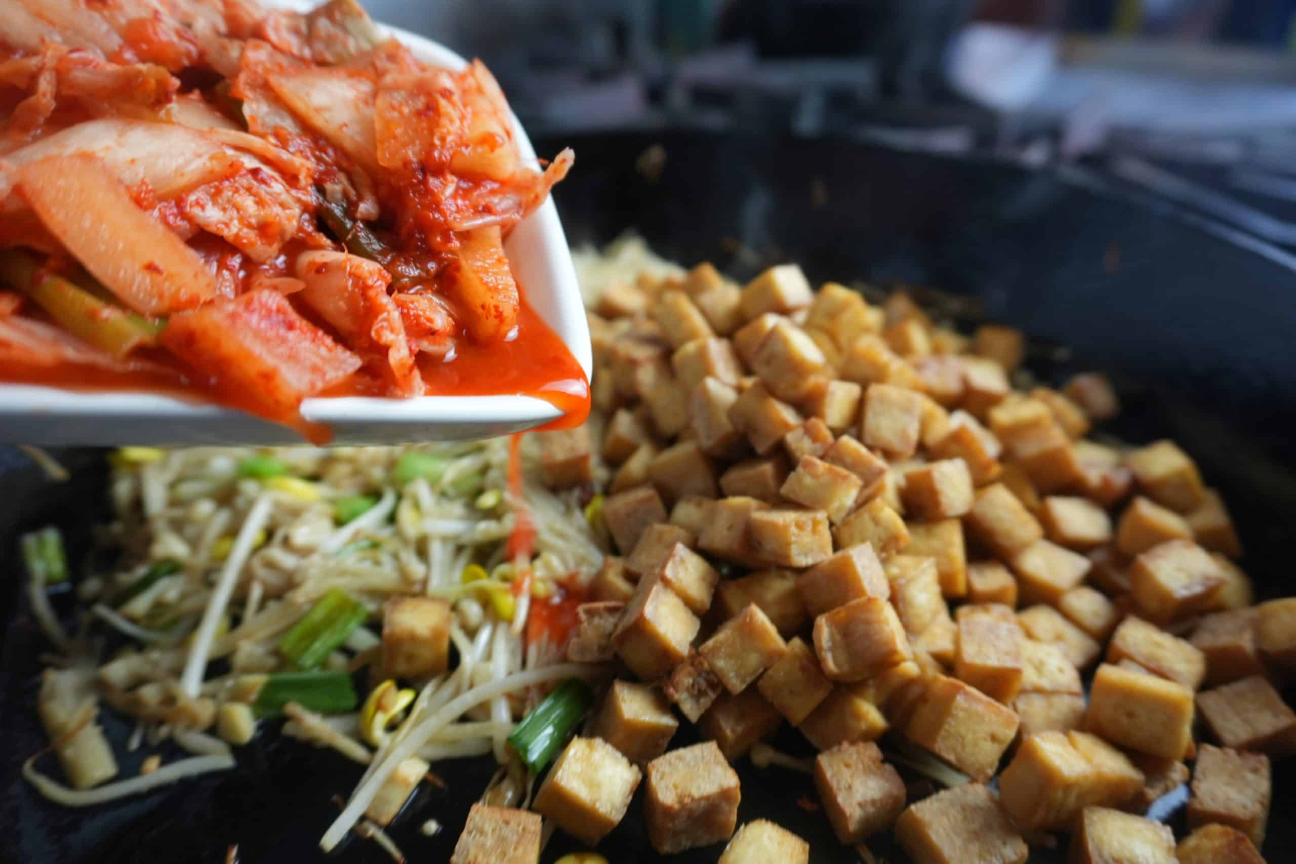 Kimchi getting added to the pan along with cubes of roasted tofu.