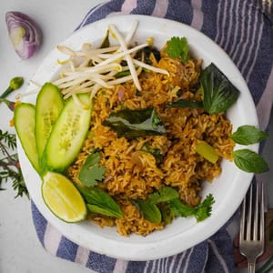 Thai fried rice in a white bowl with cucumbers and limes.