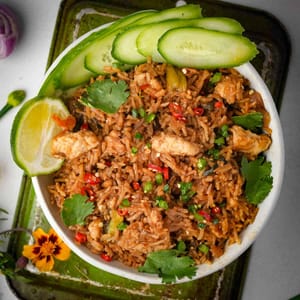 Thai fried rice in a white bowl garnished with cucumbers.