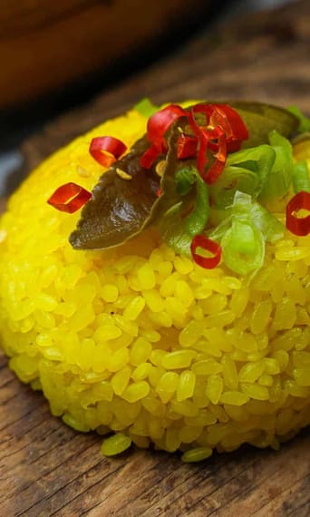 A mound of garnished yellow rice on top of a wooden board.