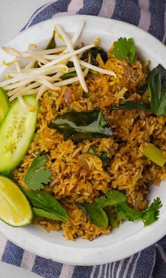 Thai fried rice in a white bowl with cucumbers and limes.