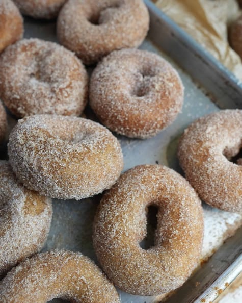 Vegan apple cider donuts coated in cinnamon and sugar on a tray.