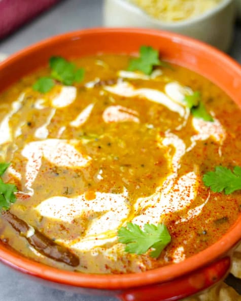 Red lentil dahl in an orange bowl. basmati rice in the background.