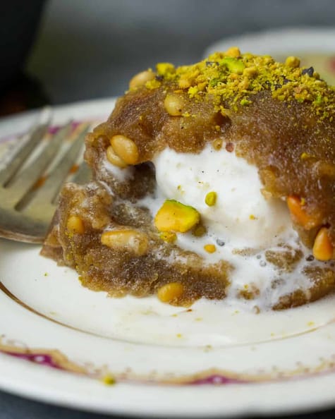 A molded mound of vanilla ice cream filled Irmik helvasi garnished with pistachios on a decorative ceramic plate.