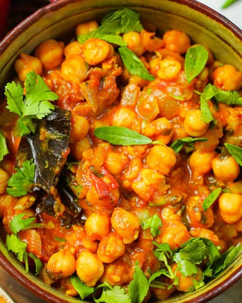 a green ceramic bowl of chana masala with tomatoes and spices garnished with methi and cilantro.