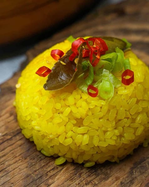 A mound of garnished yellow rice on top of a wooden board.