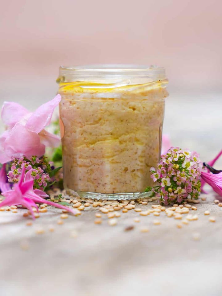 goma dressing in a glass jar surrounded by edible flowers and sesame seeds.