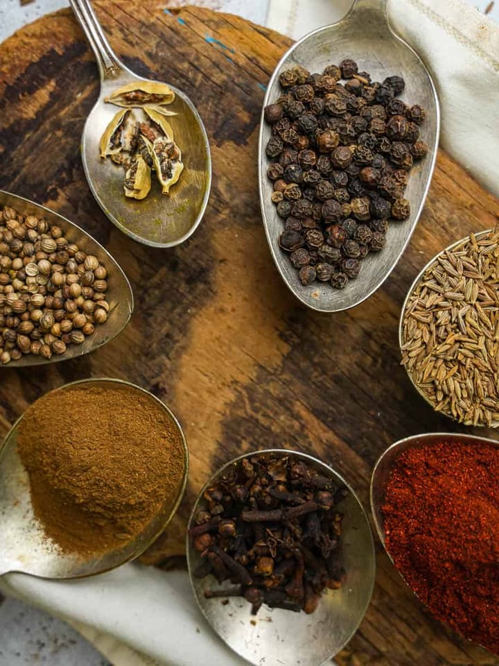 Spices in spoons on a wooden cutting board.