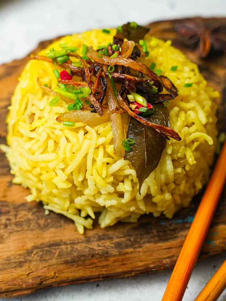 A plate of yellow nasi minyak rice with chopsticks on a wooden cutting board.