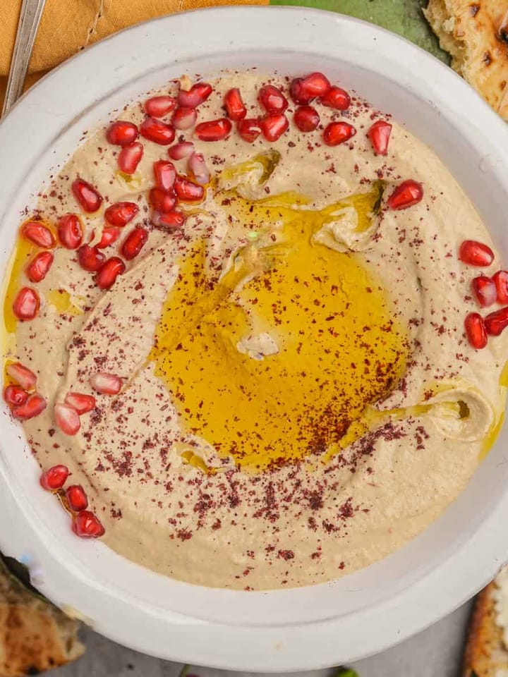 A bowl of mutabal with olive oil and pomegranate seeds.