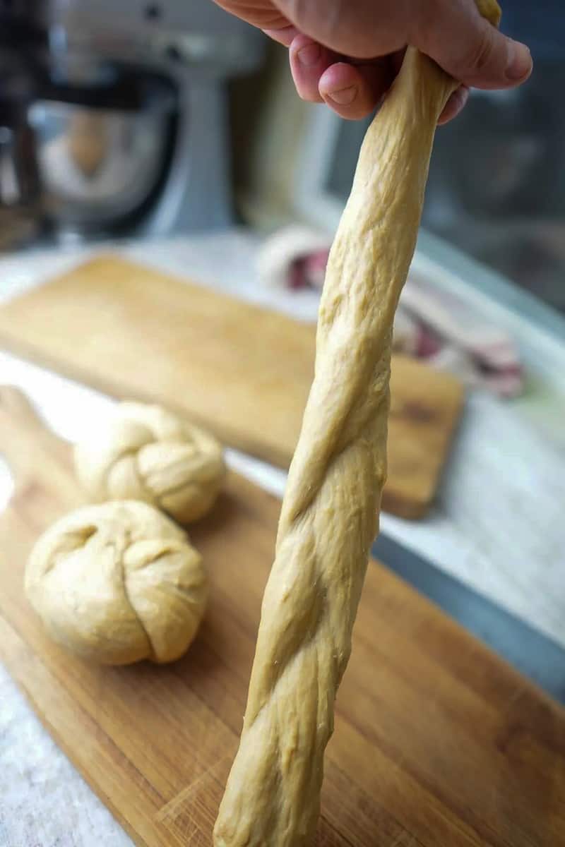 Hands stretching the braided seitan dough into a longer rope shape.