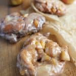 A few vegan apple fritters with a hot mug of coffee and apple in the background
