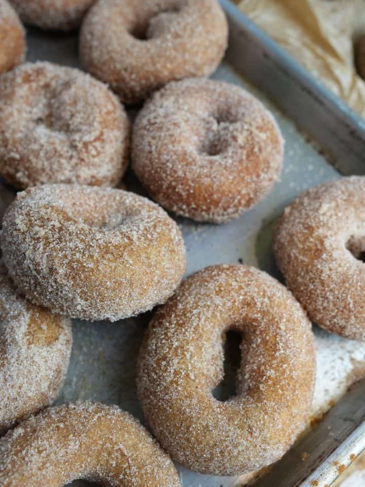 Vegan apple cider donuts coated in cinnamon and sugar on a tray.