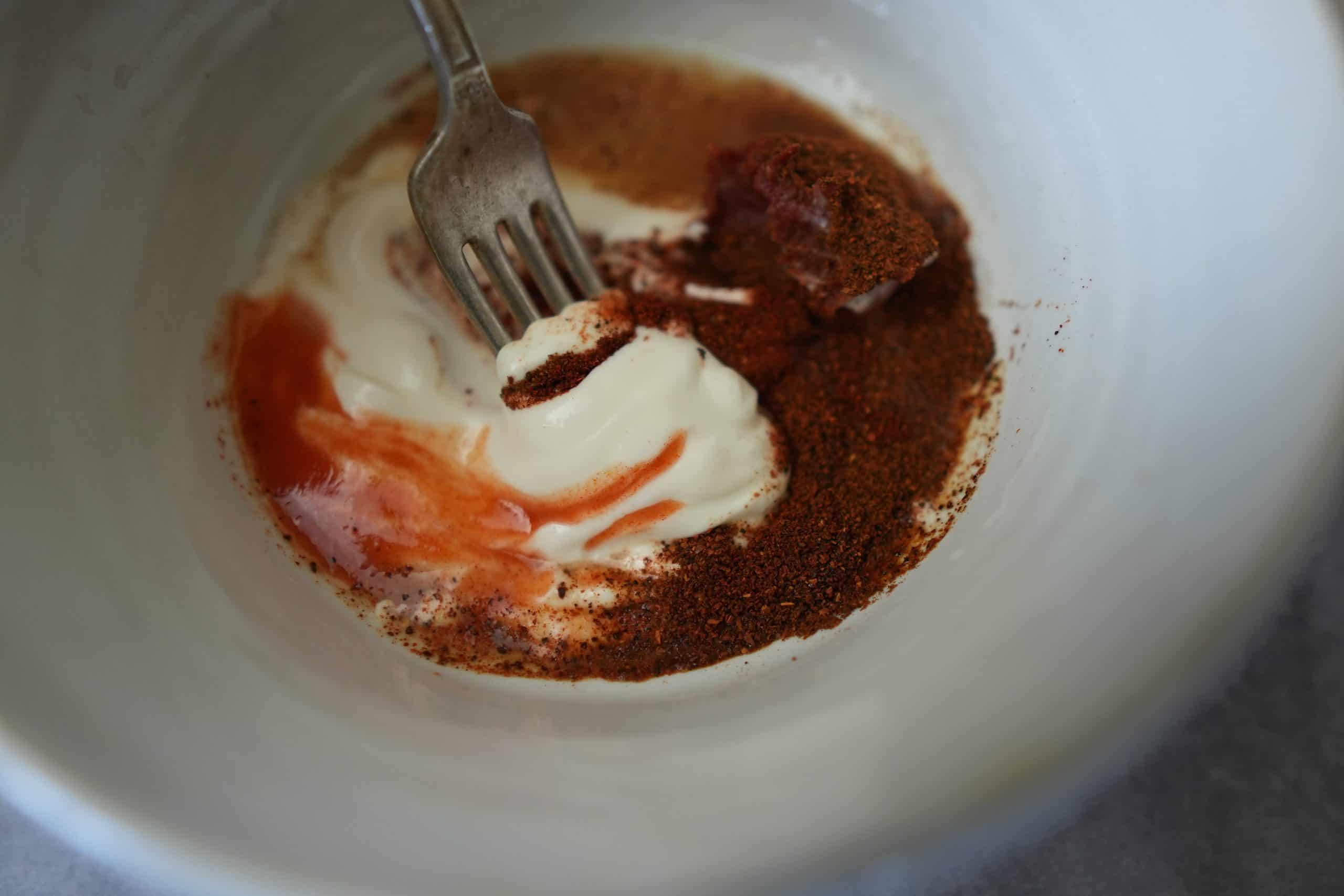 ancho chili mayo being mixed up in a small white bowl using the tines of a fork.