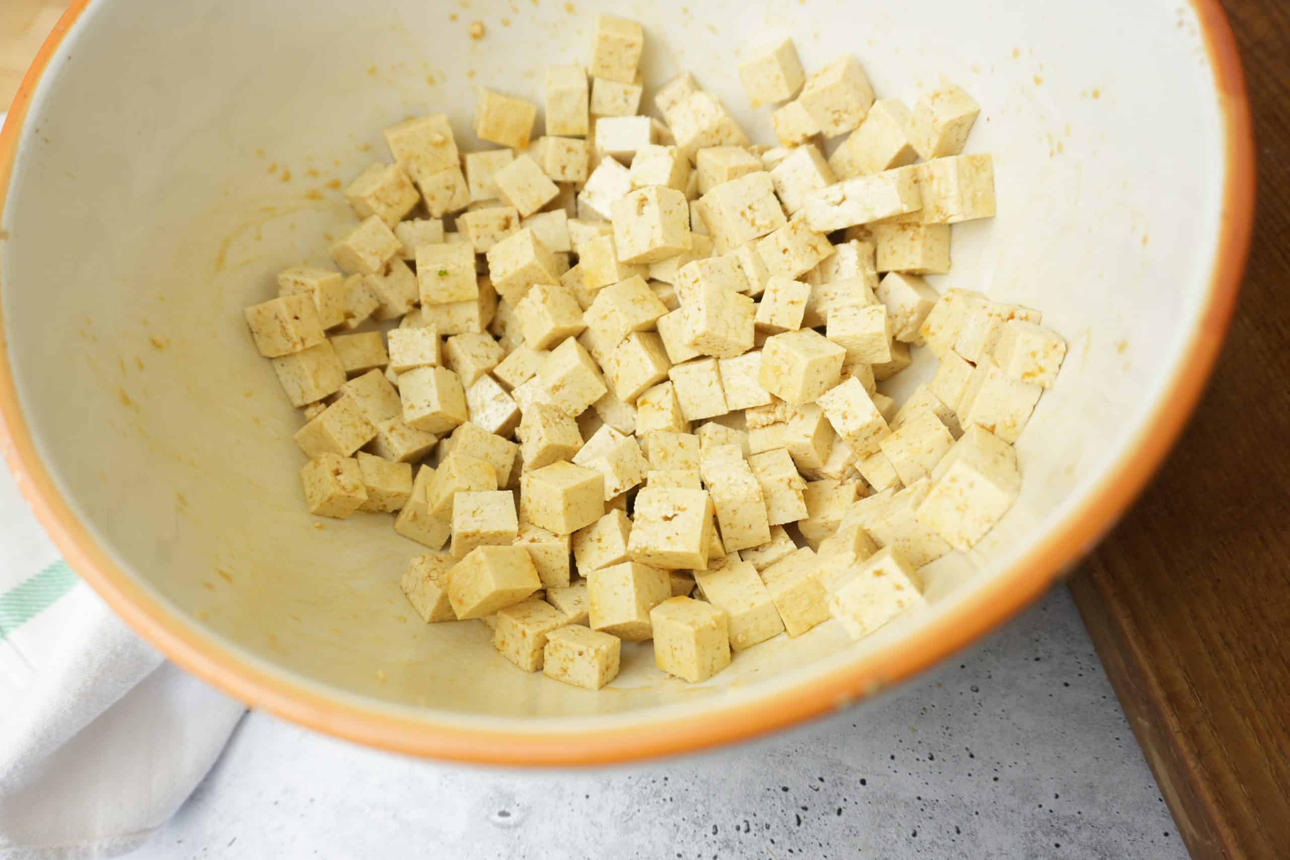 Seasoned cubes of tofu in a white ceramic bowl ready to be roasted in the oven.