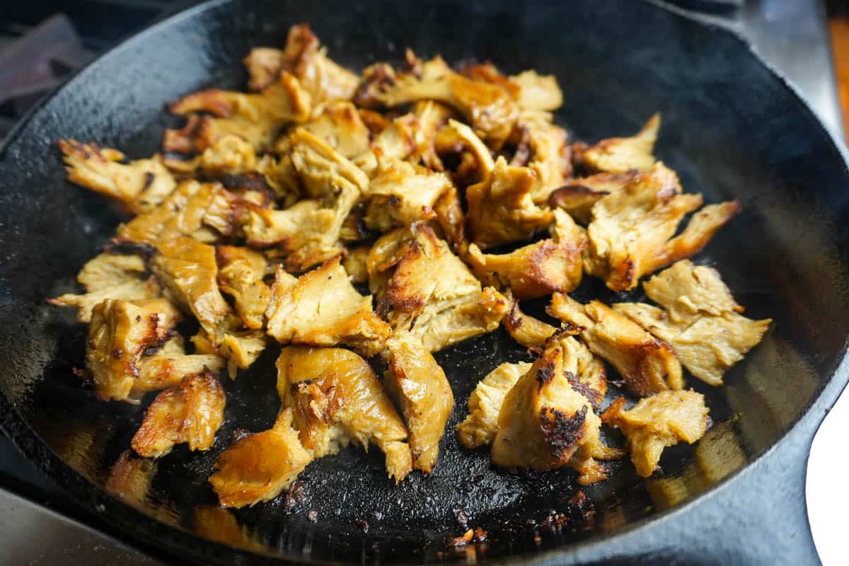 seitan being stir fried in a large cast iron skillet. you can see the pieces becoming browned with crispy edges.