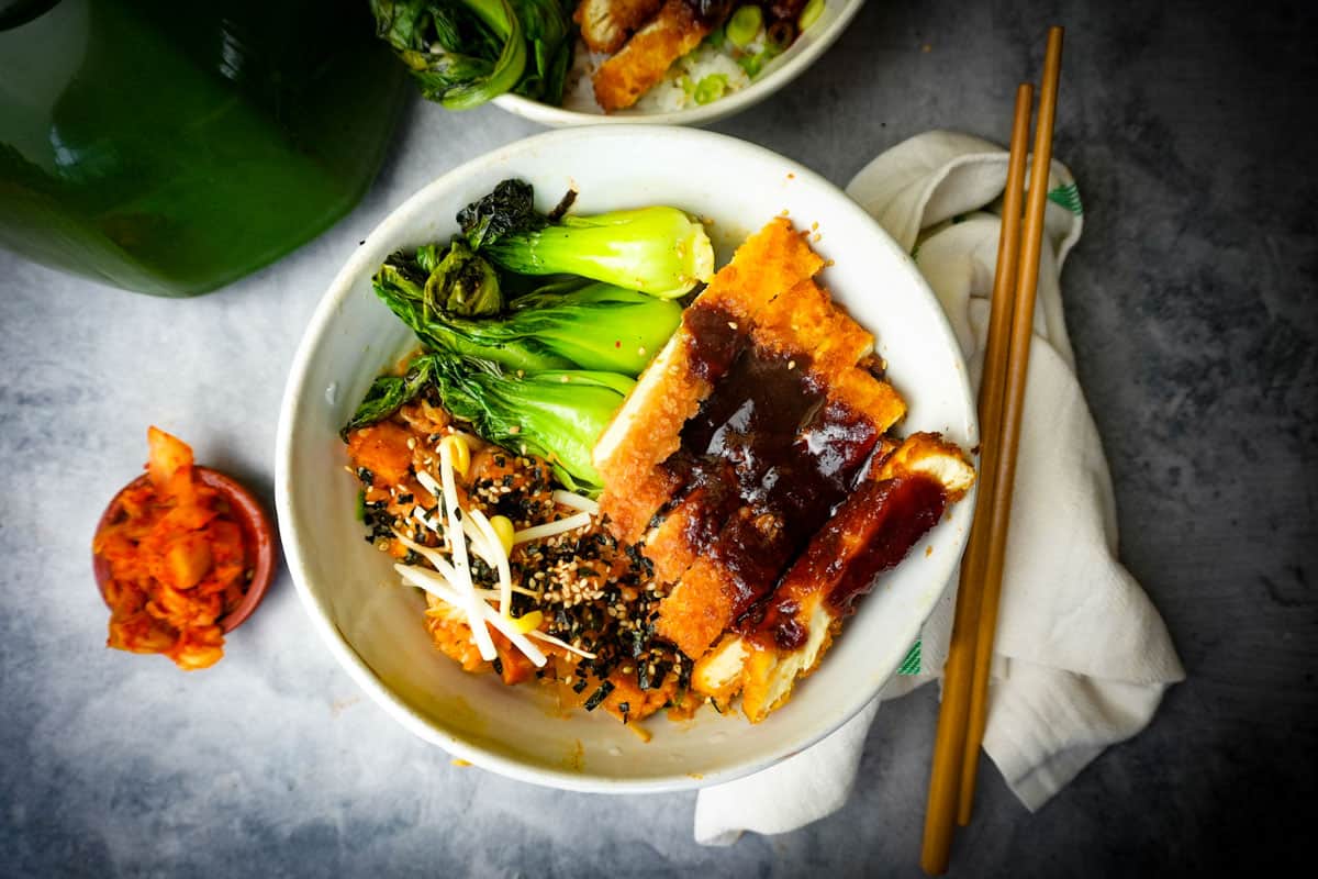 Tofu katsu in a white bowl with steamed bok choy and kimchi fried rice. chopsticks on the side