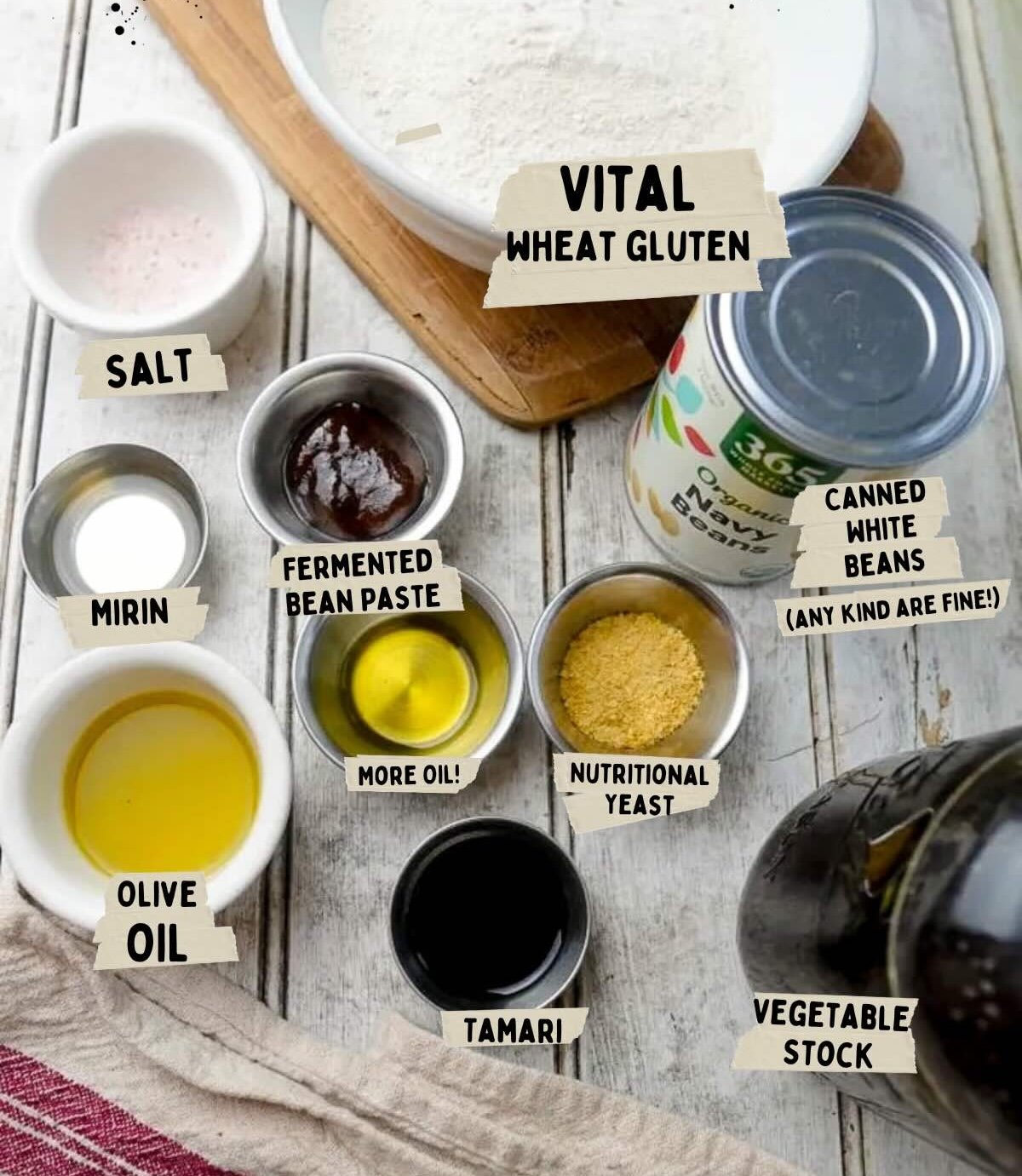 Ingredients on a table for a recipe to create vegan chicken. Includes salt, mirin, olive oil, tamari, fermented bean paste, nutritional yeast, vegetable stock, canned white beans, and vital wheat gluten.