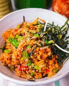 vegan kimchi fried rice in a white bowl. Napkin underneath the bowl. Teacup and pitcher and a jar of kimchi in the background
