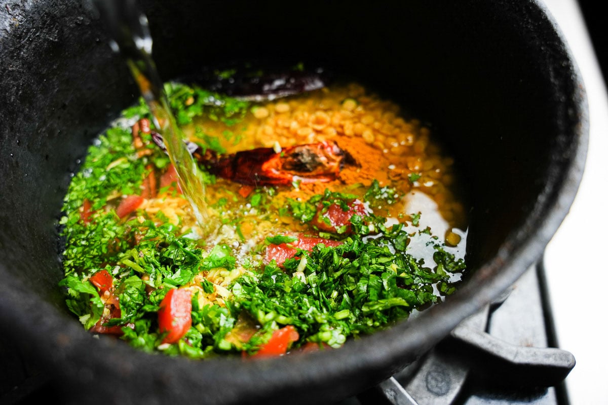 Adding water to cook the dal in a black metal pot.