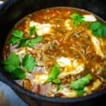 Harira garnished with fresh herbs and yogurt in a small black pot.
