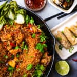 Pad woon sen in a pan with dumplings, a lime, and chopsticks on the table.