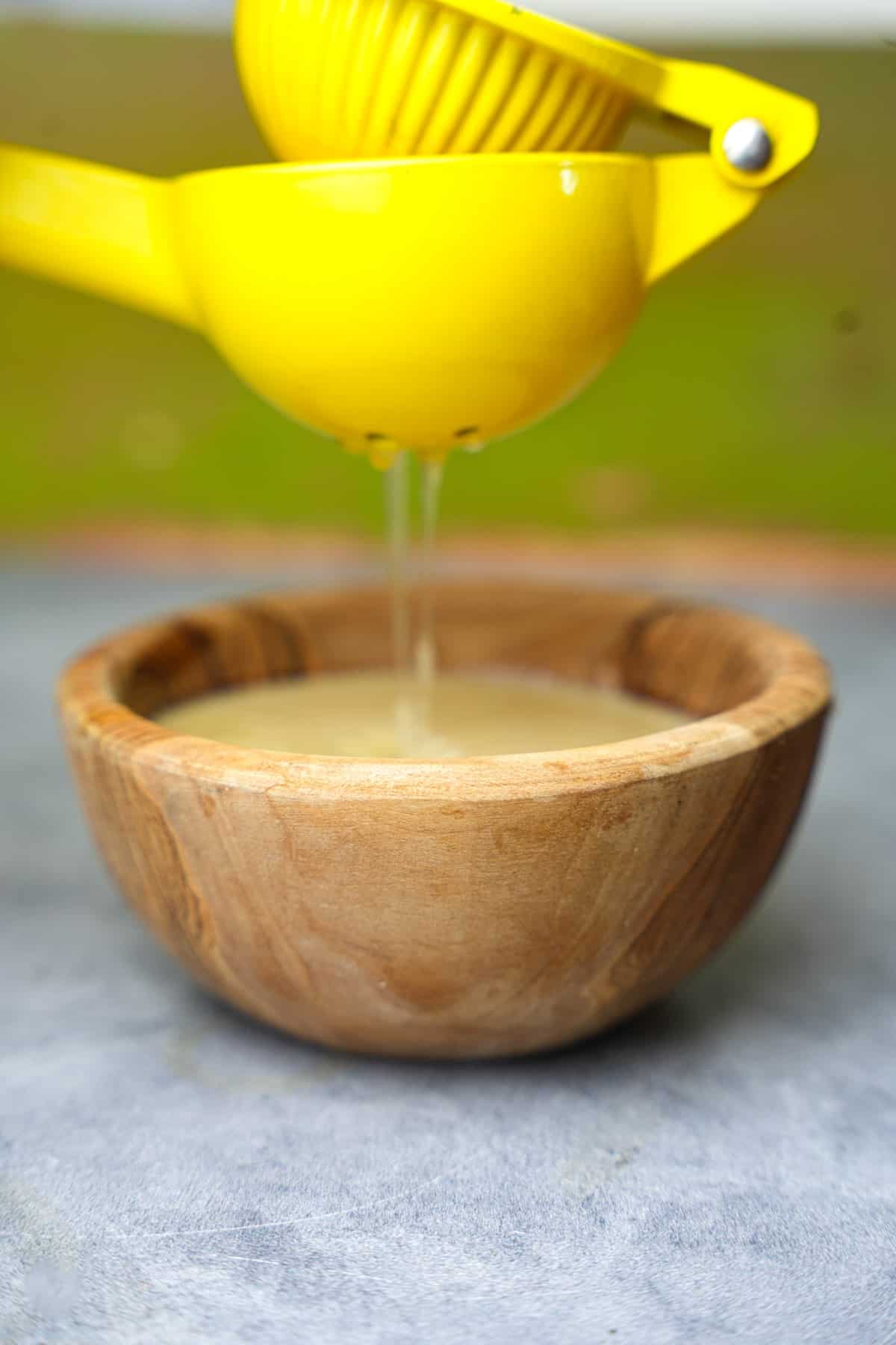 Lemon juice is added to tahini sauce in a wooden bowl.