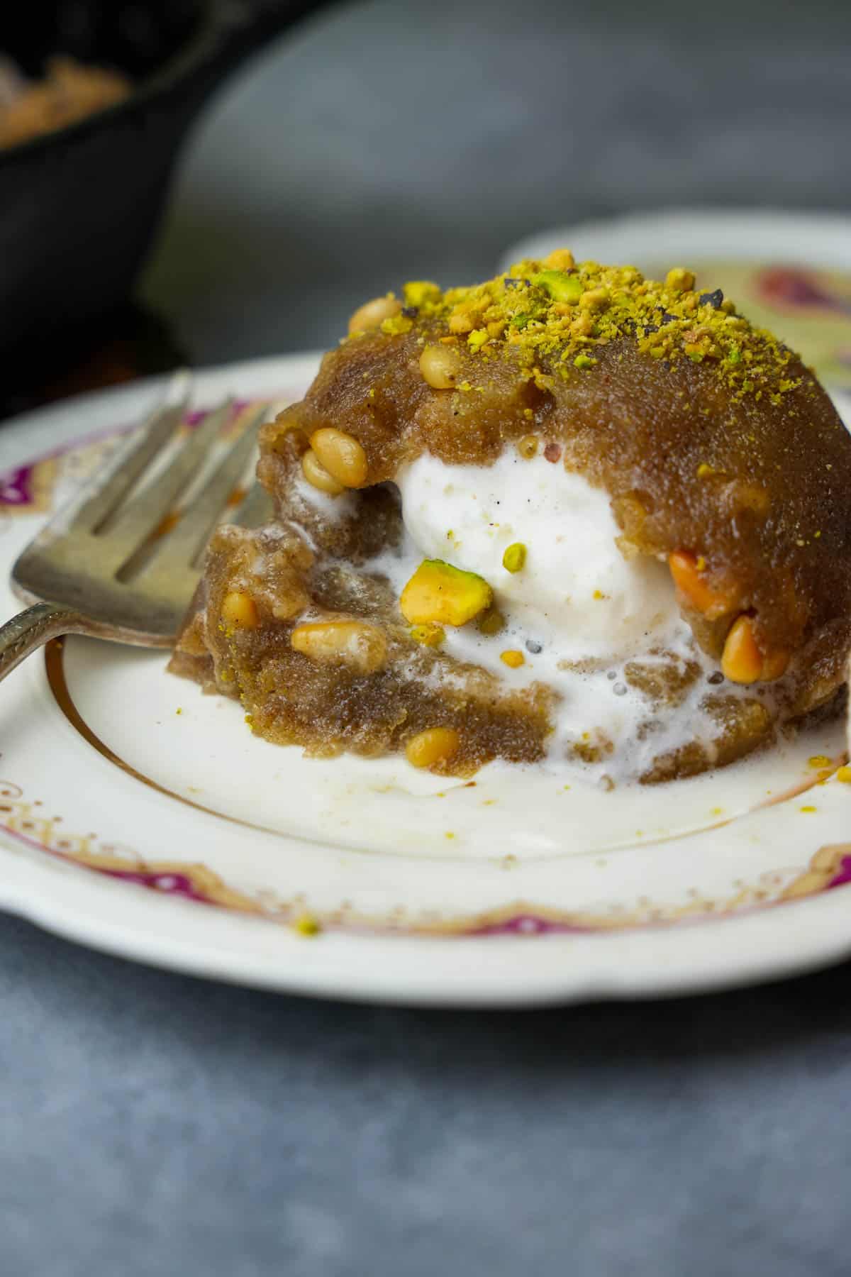 A molded mound of vanilla ice cream filled Irmik helvasi garnished with pistachios on a decorative ceramic plate.