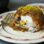 A molded mound of vanilla ice cream filled Irmik helvasi garnished with pistachios on a decorative ceramic plate.
