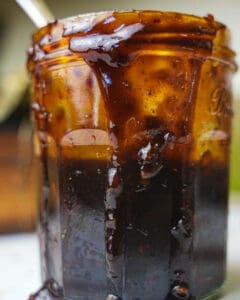 A glass jar dripping with korean bbq sauce with a spoon in it on a white wooden surface.